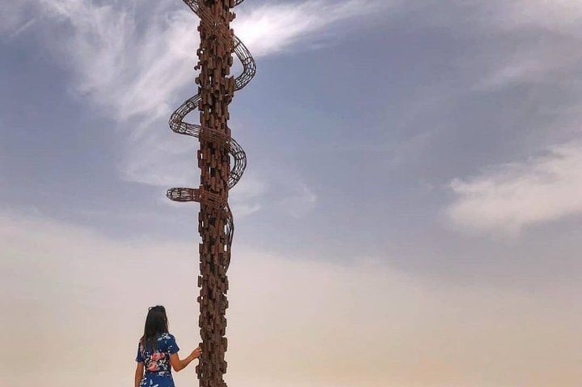 Une personne se tient à côté d’une grande sculpture métallique torsadée, sur fond de ciel nuageux. 3