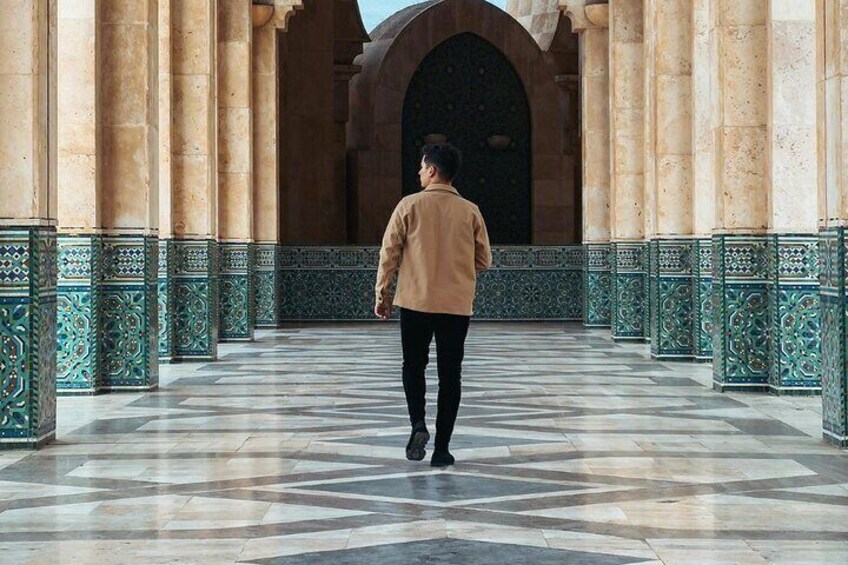 A person walking through a corridor with patterned tiles and ornate columns. 2