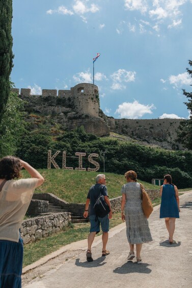 A group of people walking on a path with a historic fort and the word 'KLIS' in the background. 2