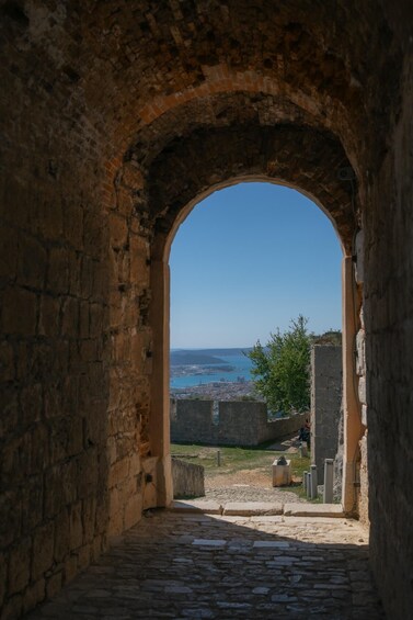 An arched stone doorway leading to a coastal view with a clear sky. 3