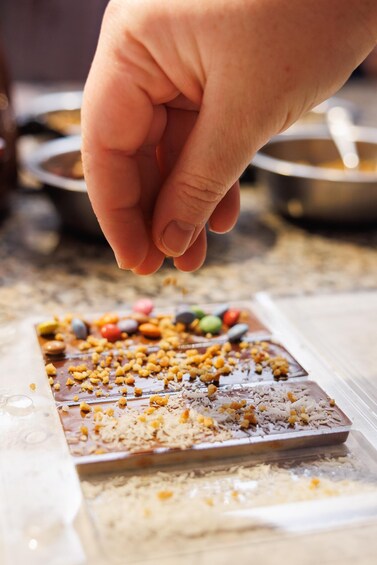 A hand sprinkling nuts onto a chocolate bar with candy pieces. 2
