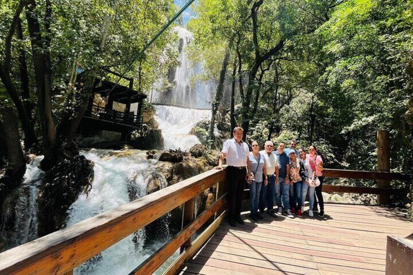 Un pont en bois enjambant une cascade, sur lequel se tient un groupe de personnes. 1