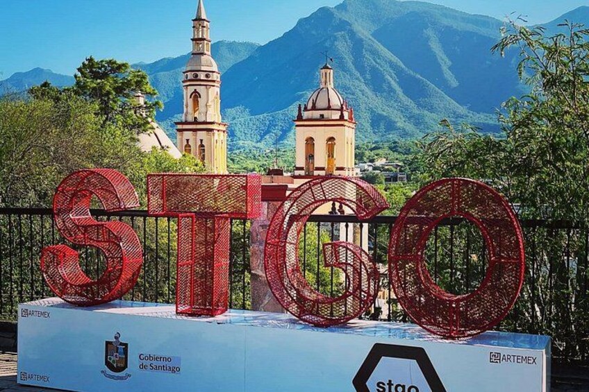 A large red sculpture spelling 'STGO' in front of a church with mountains in the background. 5