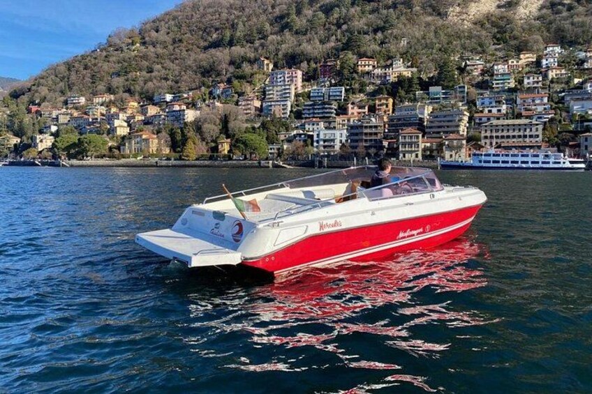 Un motoscafo rosso e bianco su acque calme, con sullo sfondo una cittadina collinare. 3