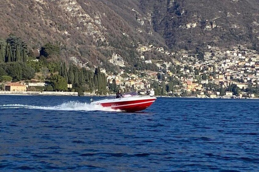 Un bateau à moteur rouge et blanc navigue sur une étendue d’eau, avec une ville située dans les montagnes en arrière-plan. 2