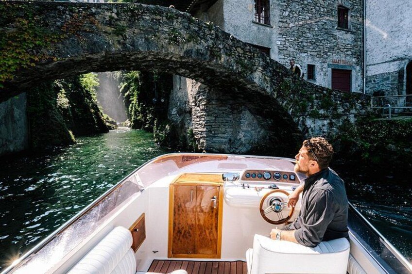 Un bateau avec une cabine en bois et une personne au gouvernail, passant sous un pont de pierre qui enjambe une rivière. 3