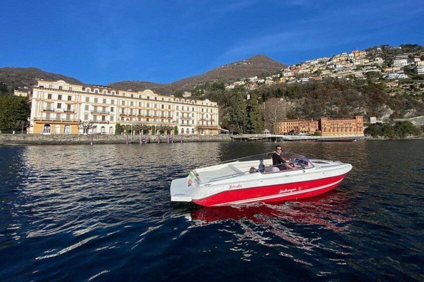 Una barca rossa e bianca su un lago, con un albergo e delle colline sullo sfondo. 2