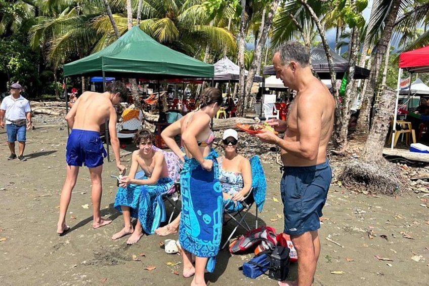 People on a sandy beach with palm trees and a green tent in the background. 5