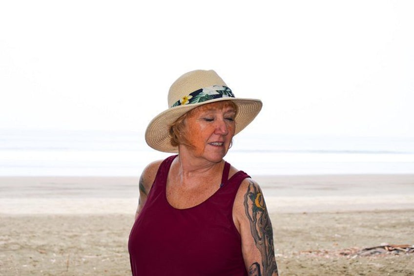 A person standing on a beach with a hat, tattoos on arms, and a tank top. 2