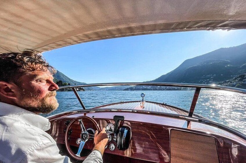 A person steering a boat on a calm lake with mountains in the background. 4