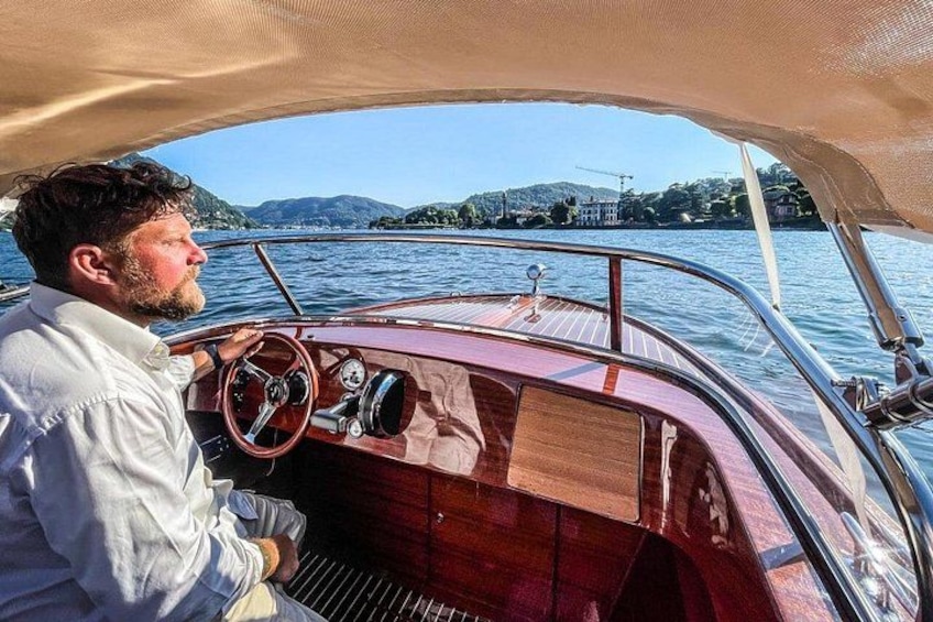 A man steering a wooden boat on a calm lake with a mountainous landscape in the background. 3