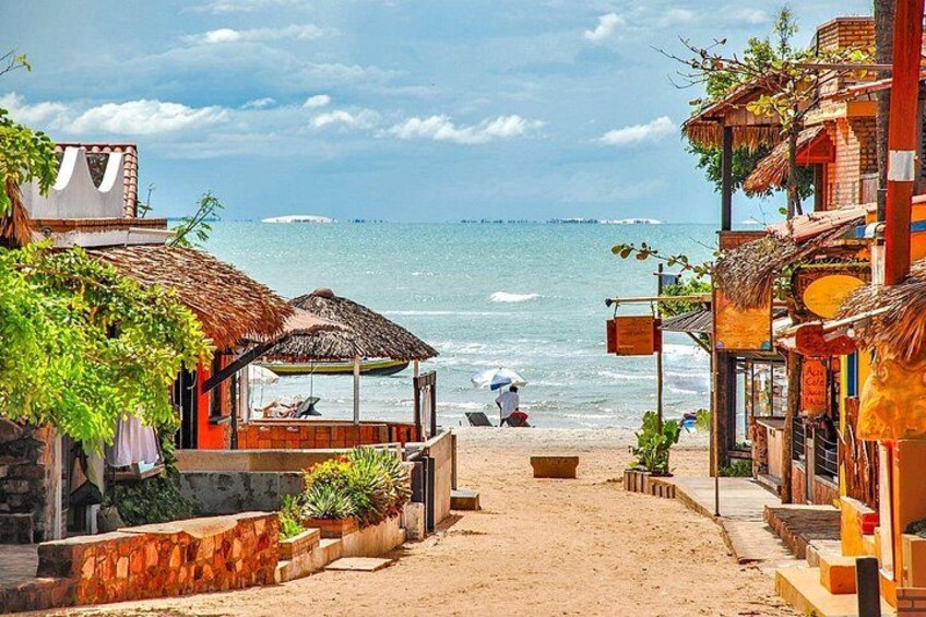 A beach with thatched-roof huts, a sandy path, and the ocean in the background. 4