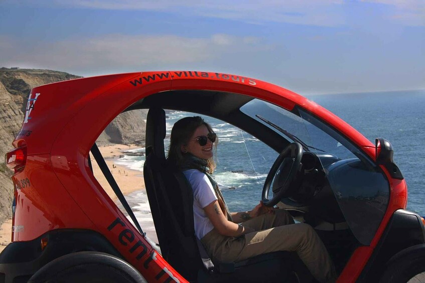 Una persona guida un veicolo rosso con la scritta 'www.villa-tour.co.nz' sul fianco, vicino a una spiaggia con scogliere e oceano. 5