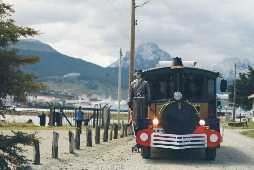 Un autobús antiguo con un conductor y un pasajero en un camino de tierra, rodeado de montañas y una cerca. 5