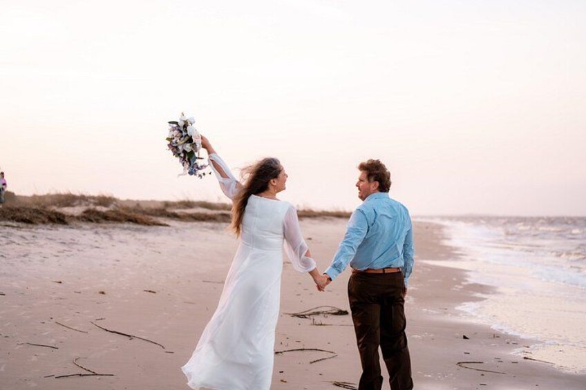 A couple holding hands on a beach with the ocean in the background. 4