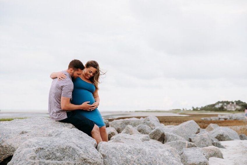A couple embracing on a rocky beach with a distant hill in the background. 2