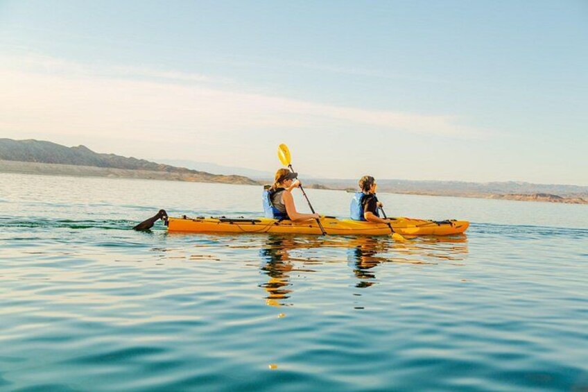 Two people kayaking on a calm body of water with distant mountains in the background. 2