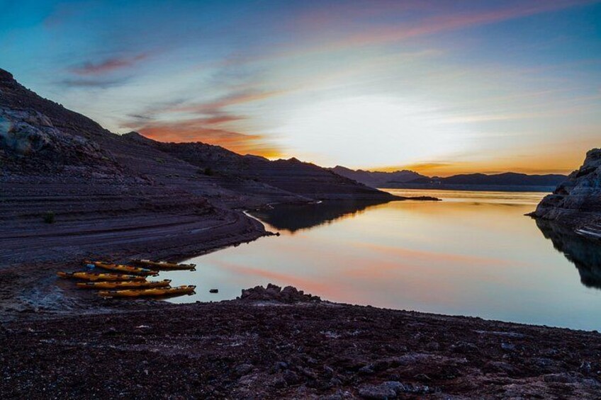 A calm lake at sunset with a clear sky, rocky terrain, and a small boat on the water. 5