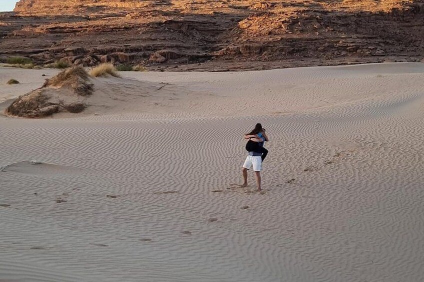Une personne se trouve dans un désert, avec des dunes de sable et des falaises rocheuses en arrière-plan. 3