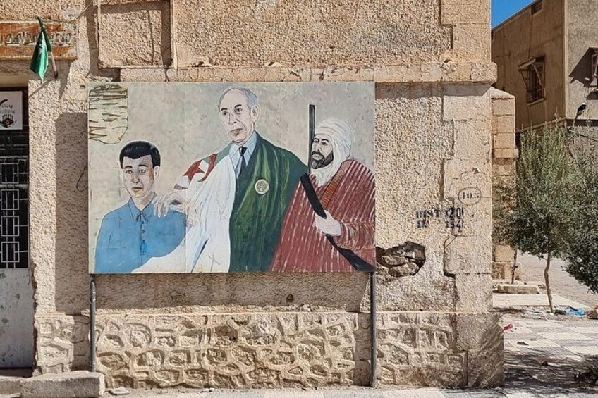 Une fresque murale sur un mur de pierre représentant trois personnages, dont l’un porte une chemise bleue et les deux autres sont vêtus de tenues traditionnelles. 5