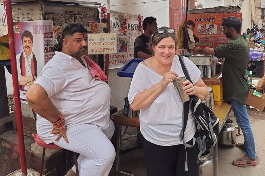 Two people standing in a market area with various signs and stalls in the background. 4