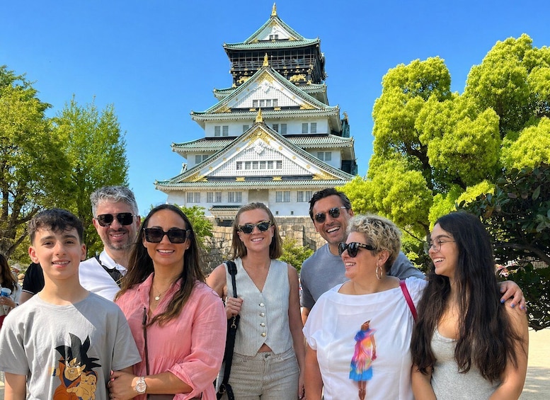 A group of people in front of a traditional Japanese castle with a multi-tiered roof and golden accents. 3