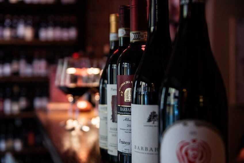 A row of wine bottles with labels, some with text and others with images, in a dimly lit setting. 3