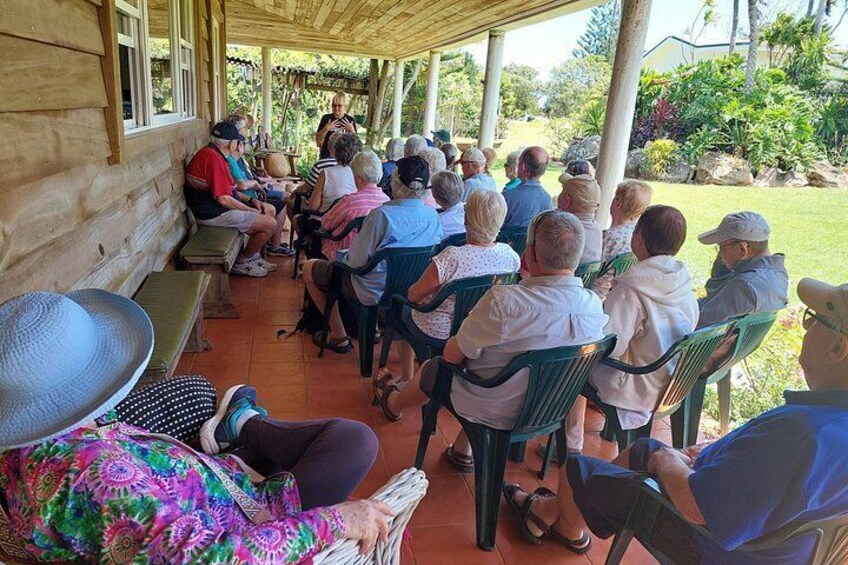 A group of people seated outdoors on chairs, facing a speaker. 2