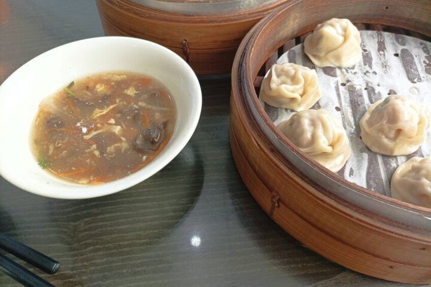 A bowl of soup and a steamer with dumplings on a table. 3