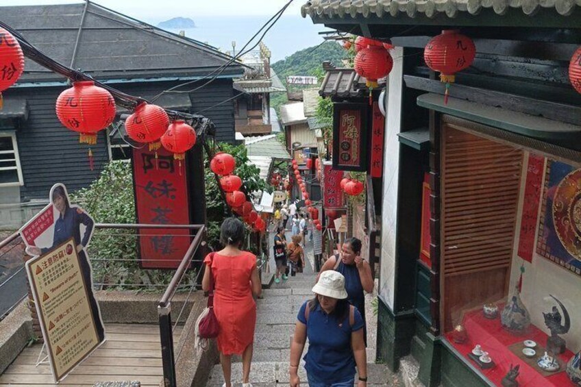A narrow street with red lanterns, traditional buildings, and a signboard. 2