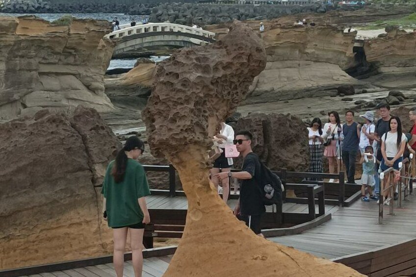 A rocky landscape with a wooden boardwalk, a bridge, and people walking. 4