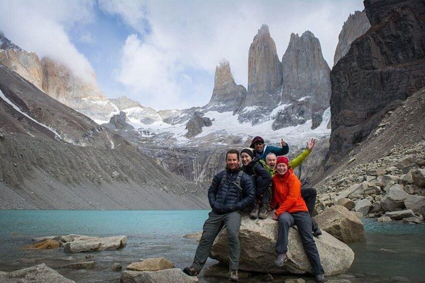 A group of people on a rocky outcrop by a turquoise lake with snow-capped mountains in the background. 2
