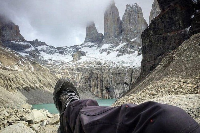 A person's legs and feet in hiking boots, with a mountainous landscape and a lake in the background. 3