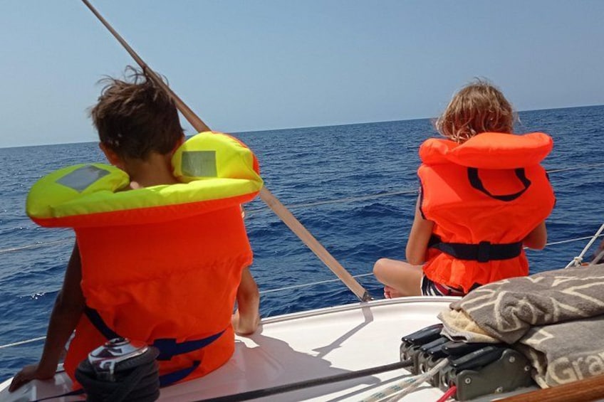 Two people on a boat wearing orange life jackets, with the ocean in the background. 3