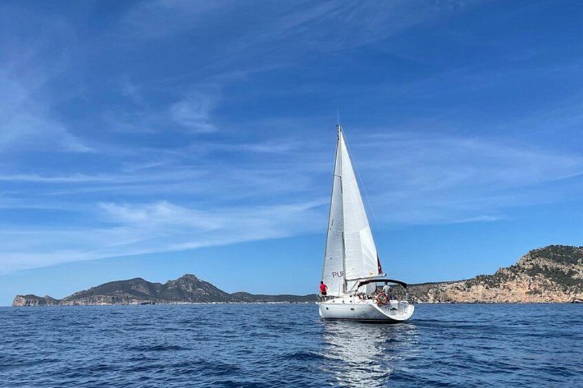 A sailboat on a calm sea with a clear sky and distant rocky coastline. 3