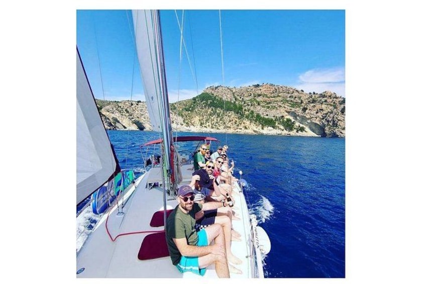 A sailboat with people on board, a rocky coastline, and clear blue water. 2