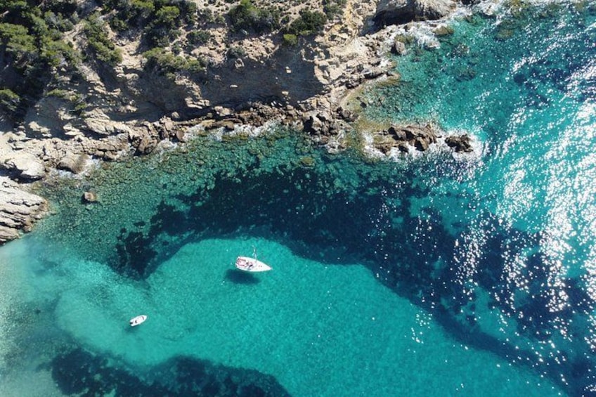 A coastal area with clear turquoise waters, rocky terrain, and a small boat anchored near the shore. 2
