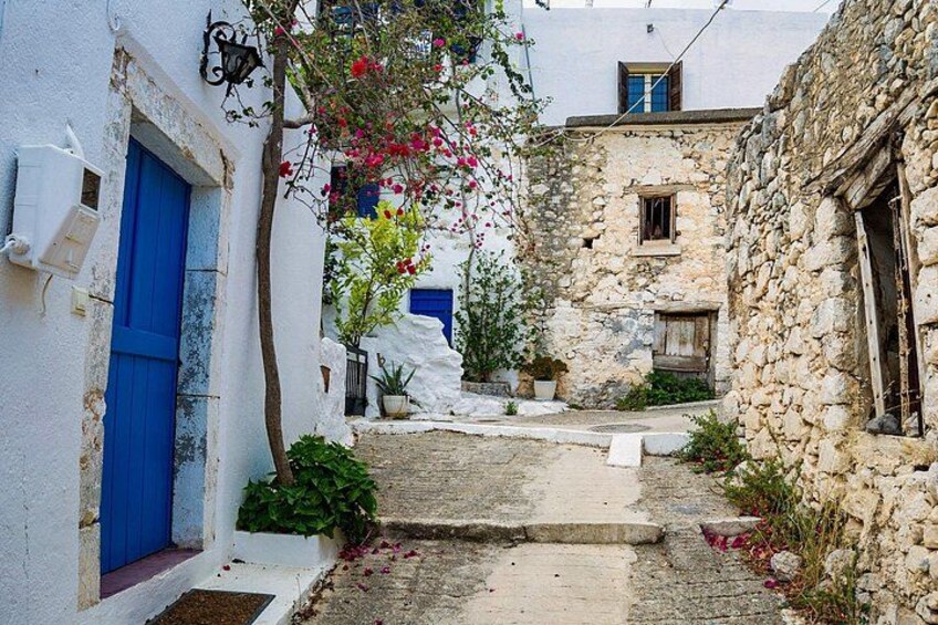 A narrow cobblestone street flanked by white buildings with blue doors and stone walls. 2