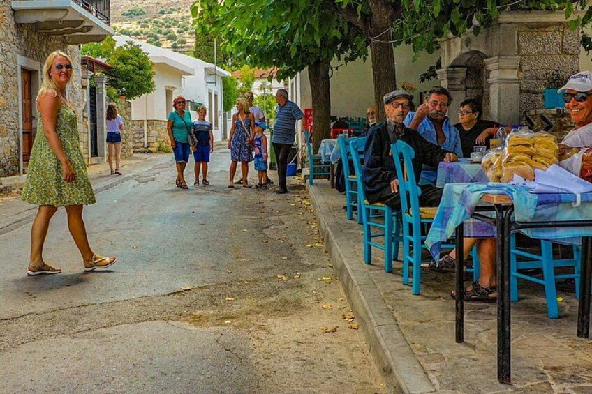 A street with people sitting at tables, a woman walking, and buildings in the background. 5
