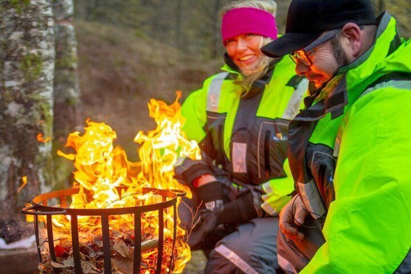 Två personer sitter vid ett lägerbål i en skog. 2
