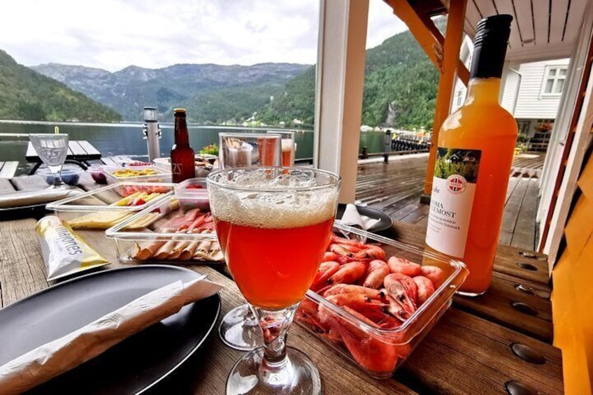 Ett bord med en drink, några snacks och en flaska apelsinjuice på en båt, med en sjö och berg i bakgrunden. 5