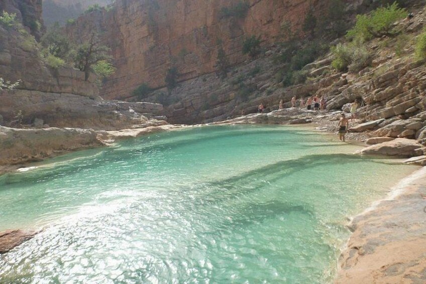 A turquoise pool surrounded by rocky cliffs and sparse vegetation. 2