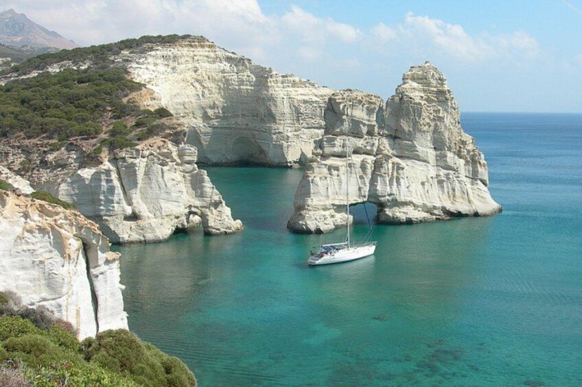 A coastal landscape with white cliffs, clear turquoise waters, and a sailboat anchored near the shore. 2