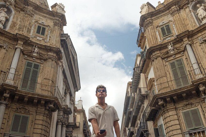 A person standing between two historic buildings with ornate facades and columns. 1