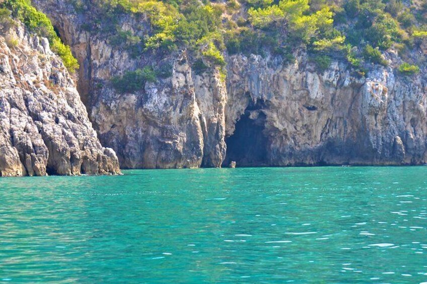 A coastal cliff with a cave entrance and turquoise water. 2