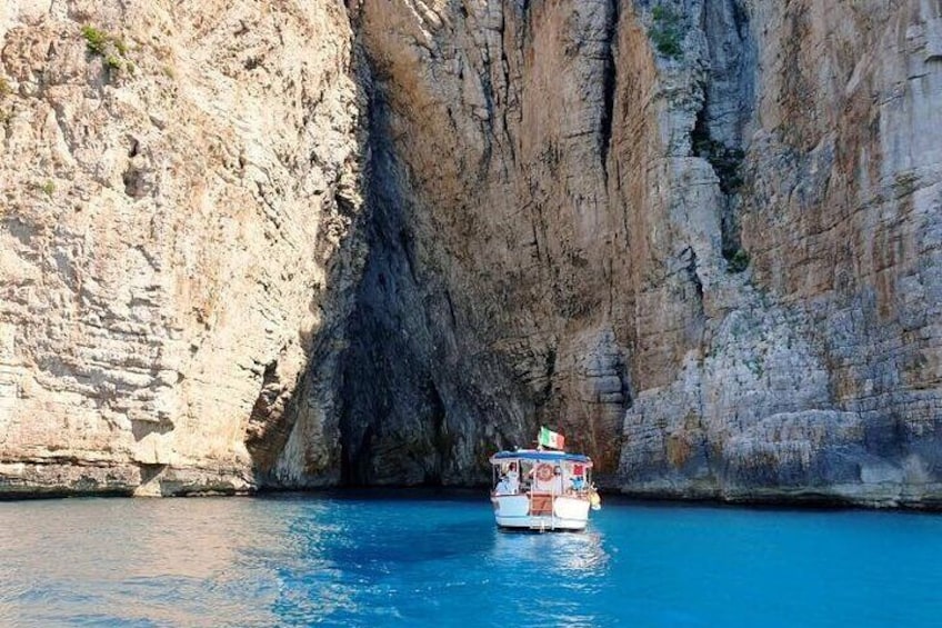 A boat with a flag on a blue body of water surrounded by cliffs. 1