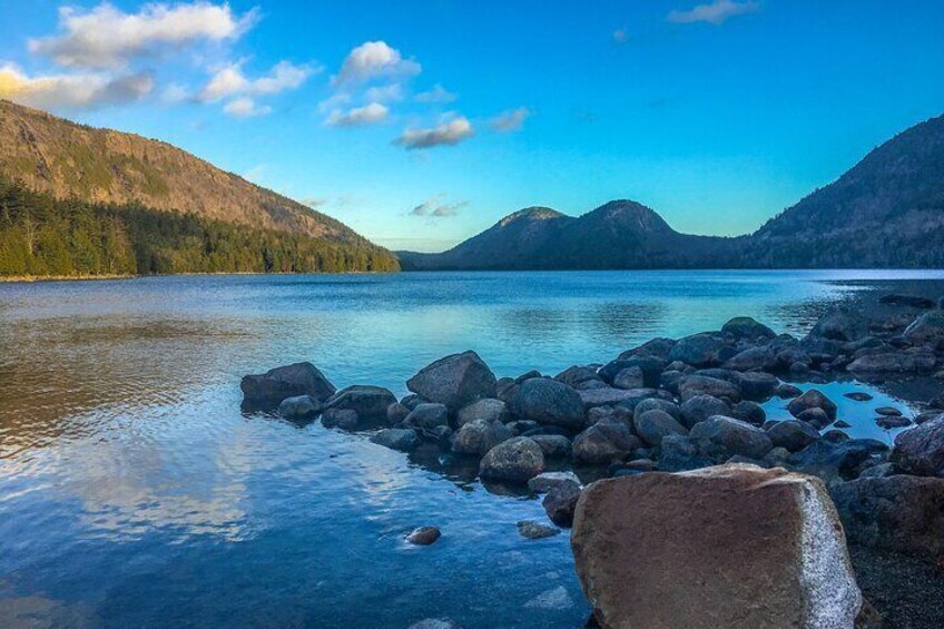 Ein ruhiger See mit großen Felsen im Vordergrund und Bergen im Hintergrund. 2