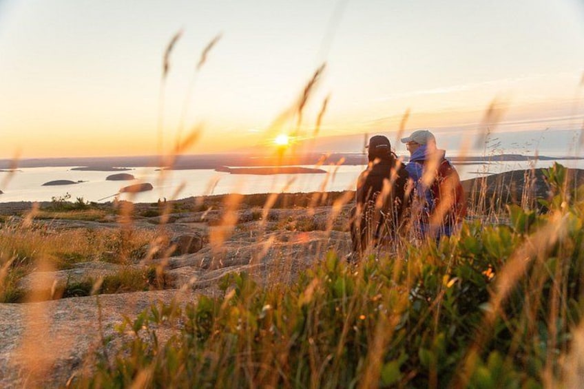 Deux personnes se tiennent debout sur un promontoire rocheux, surplombant une étendue d’eau au coucher du soleil. 5