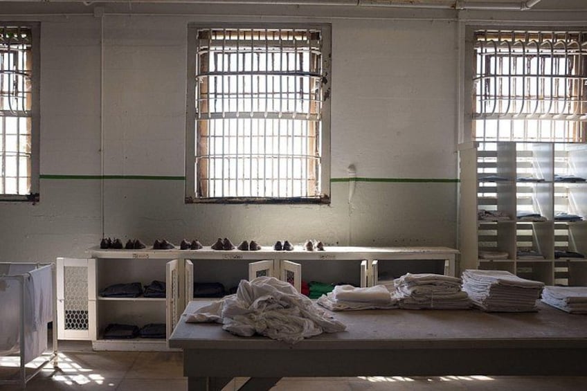 A room with barred windows, a table with folded clothes, and a shelf with shoes. 2