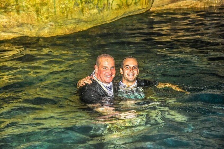 Twee personen in helder water met een rotsachtige grot op de achtergrond. 4